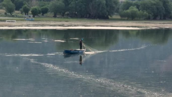 一个在湖上钓鱼的农民在早晨的黎明中反射，一个以钓鱼为生的人，一个在湖中央独自钓鱼的人，钓鱼是一种爱好