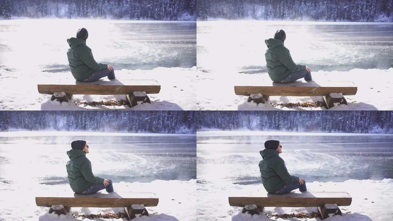 年轻人坐在白雪皑皑的湖边附近的木凳上欣赏美景