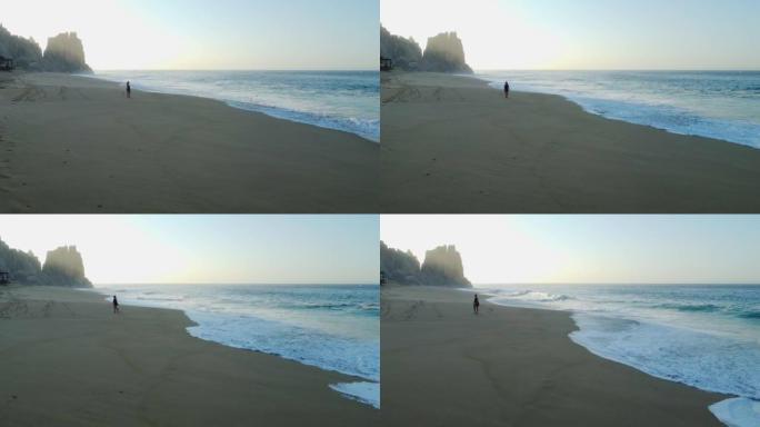 空中无人机拍摄了一名妇女在日出时沿着沿海度假胜地海滩行走的镜头