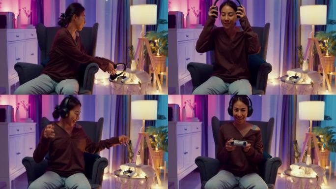 快乐的亚洲女人，休闲地坐在沙发椅上，戴着耳机和操纵杆控制器看着相机，激动人心的时刻准备晚上在客厅家里