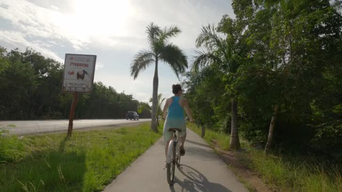 女人沿着丛林小路骑自行车，在马路旁边