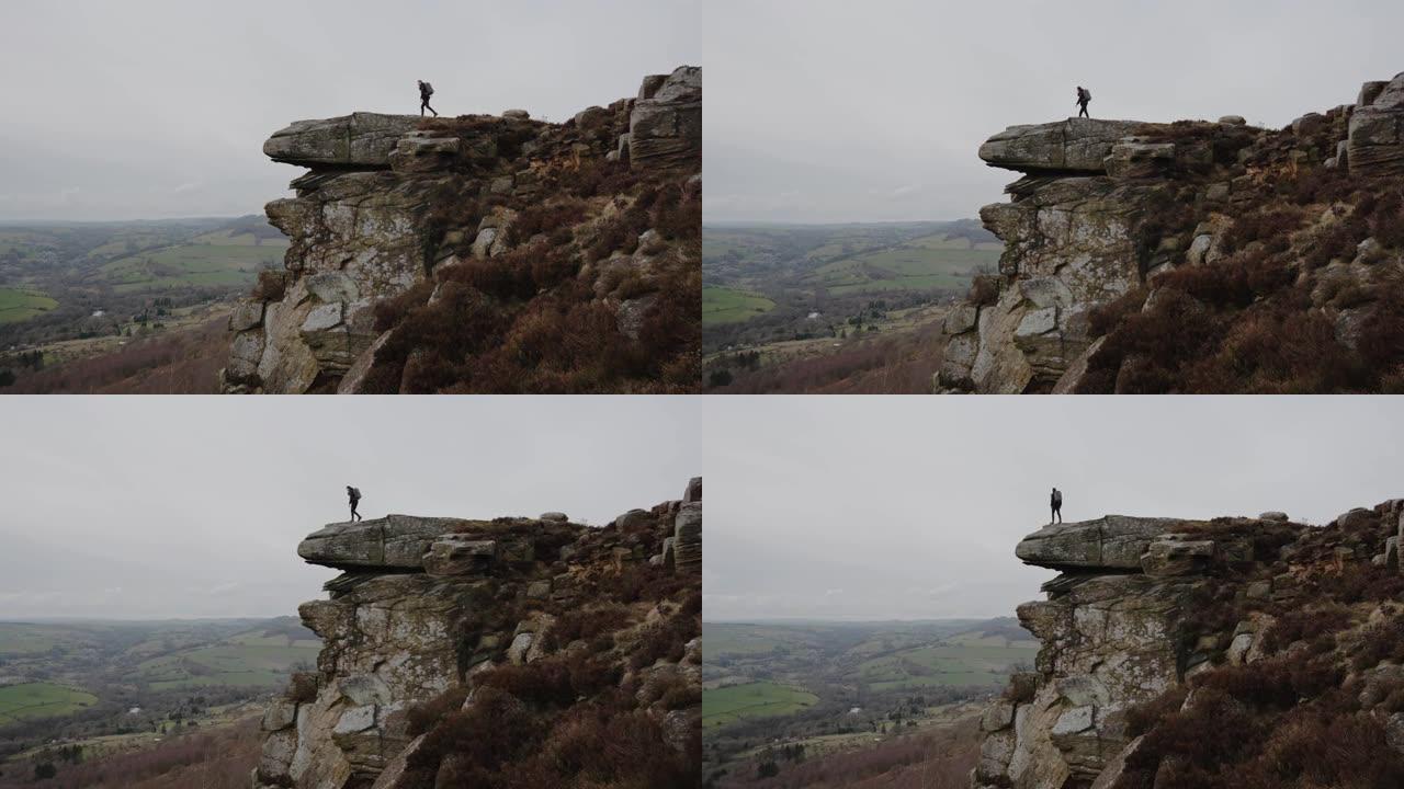 孤独的男性徒步旅行者站在岩石海角上，望着