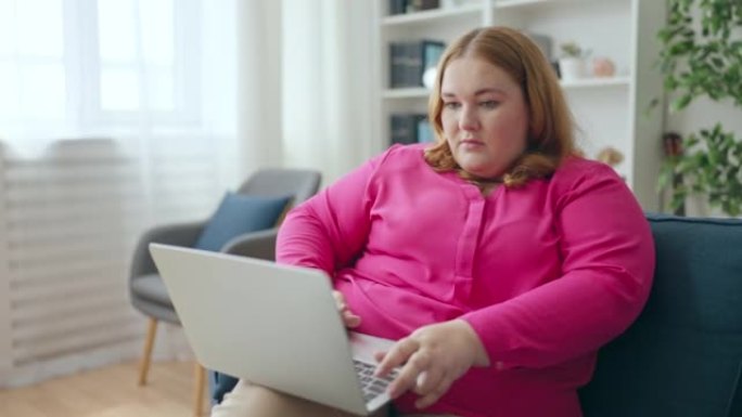 忙碌的大码年轻女子在家工作，在笔记本电脑上打字，自由职业