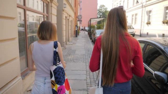 漂亮的年轻女性朋友走在城市的人行道上，互相交流