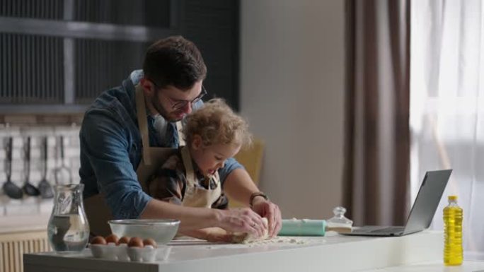 单身父亲和他的小儿子正在家里的厨房里揉面团，爸爸正在学习孩子做饭和娱乐