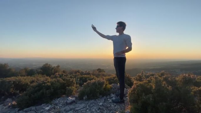 日落时站在山顶上的男子用智能手机拍照