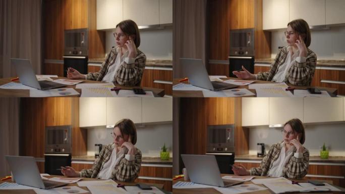 一个沉思而疲倦的女人，戴着眼镜处理财务文件，坐在工作场所使用笔记本电脑应用程序，在完成任务时看起来很
