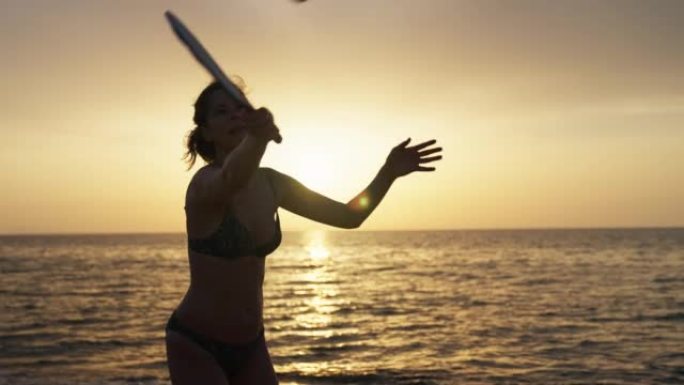 日落时在海滩上享受桨网球的女人的剪影。