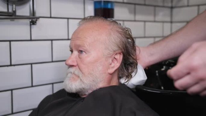 男发型师在理发店用专业洗发水洗头后，用白色毛巾擦拭客户的湿发