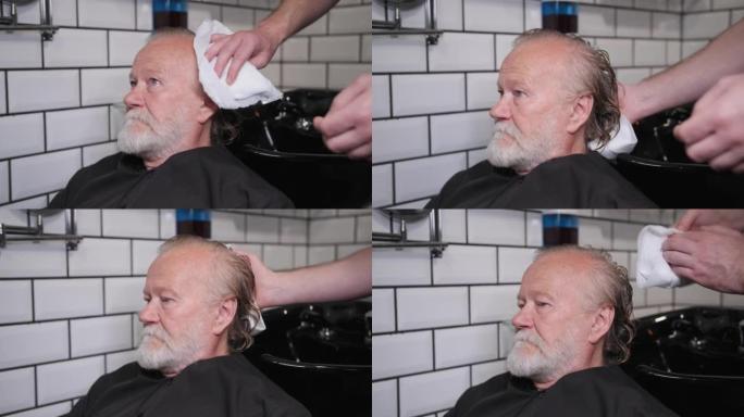 男发型师在理发店用专业洗发水洗头后，用白色毛巾擦拭客户的湿发