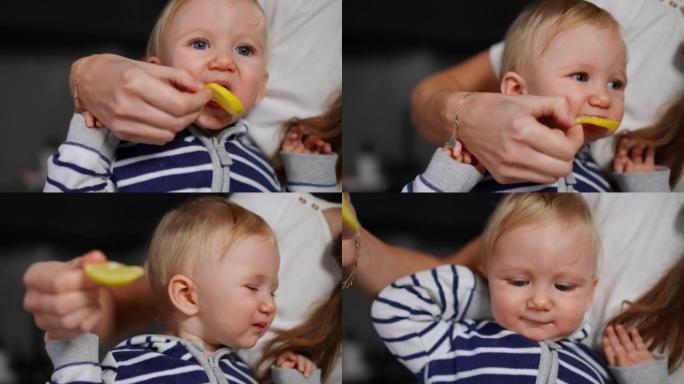 特写可爱的小女孩在无法辨认的母亲的手里咬酸柠檬。高加索父母给孩子吃柑橘类水果，作为婴儿在家中室内品尝