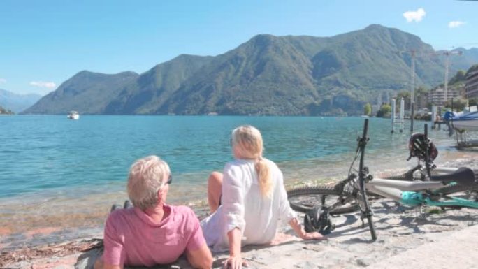 成熟的夫妇在湖岸线上的电动自行车旁放松