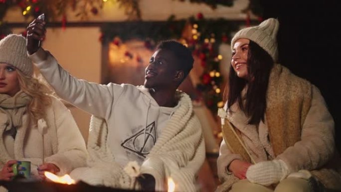 黑人男子在圣诞晚会上与朋友通过电话自拍，在篝火旁微笑着