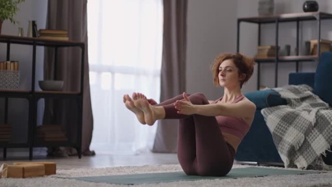 瑜伽训练健康的身体，女人拉紧腹部和腿部的肌肉，保持身体坐在地板上的平衡