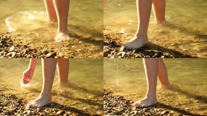男孩的腿在河里玩耍，早晨阳光照射着闪亮的水。