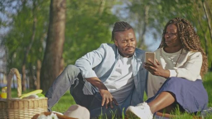 爱上非洲辫子的幸福夫妇在公园的手机上观看照片，约会