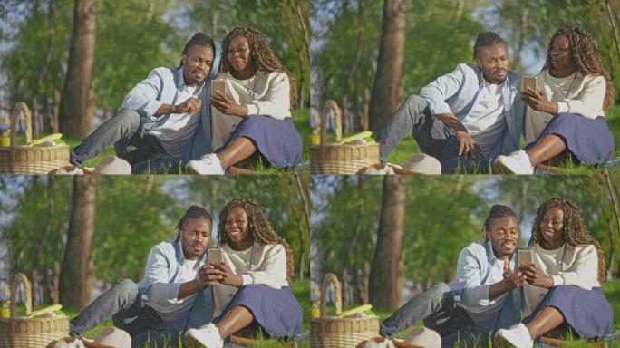 爱上非洲辫子的幸福夫妇在公园的手机上观看照片，约会