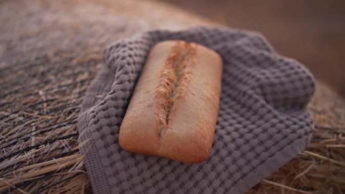 特写美味面包躺在毛巾上的黄色小麦堆户外。农村田地黑麦干草堆上美味的烘焙食品。农业和农业概念。