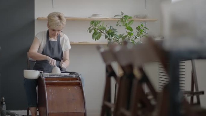 老年女工匠在陶工轮上工作，以慢动作制作粘土和陶瓷罐和盘子