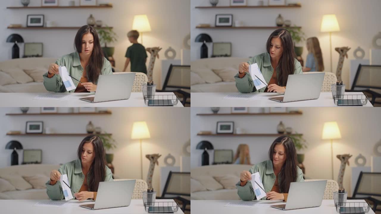 一名女商人在笔记本电脑上远程工作，并在家庭在后台唱歌时在网络摄像头上显示图表。忙碌的女商人。儿子和女