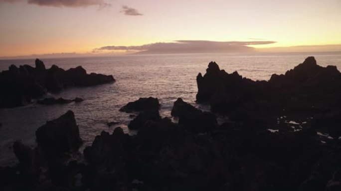 火山海岸线形成对比。黑色的岩石和夕阳在海里反射。