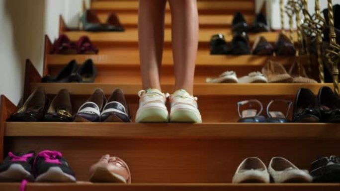 无法辨认的少女的腿走在楼梯上，鞋子停下来离开。白人自信的少年在家中室内传递鞋类。风格和购物。