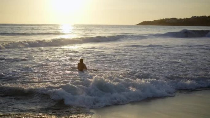 日落时男子在埃斯孔迪多港海滩冲浪