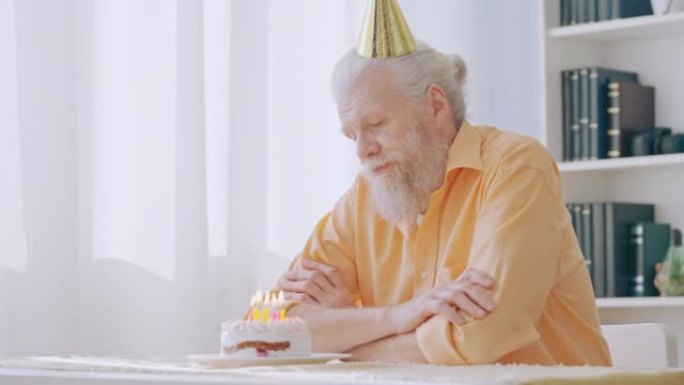沮丧的爷爷戴着派对帽独自庆祝生日，孤独的老人