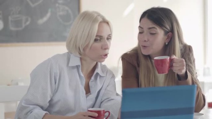 美丽微笑的白人妇女在自助餐厅喝茶或咖啡，聊天。午餐时使用笔记本电脑和聊天的正面女性朋友或同事的肖像。