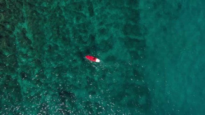 在绿松石水中，一名游泳者在桨船上的空中无人机拍摄