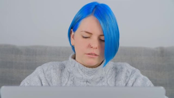 美丽的年轻成年女性，染成蓝色头发，在家工作时使用笔记本电脑