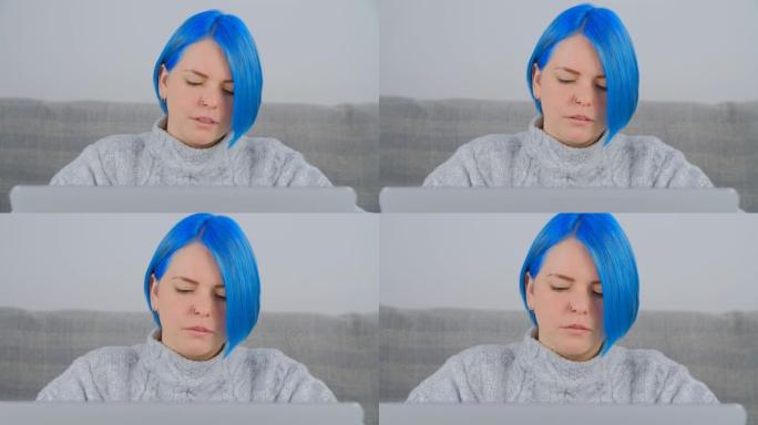美丽的年轻成年女性，染成蓝色头发，在家工作时使用笔记本电脑