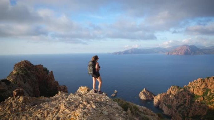 女徒步旅行者站在视线处，在日落时眺望海洋和悬崖海岸线