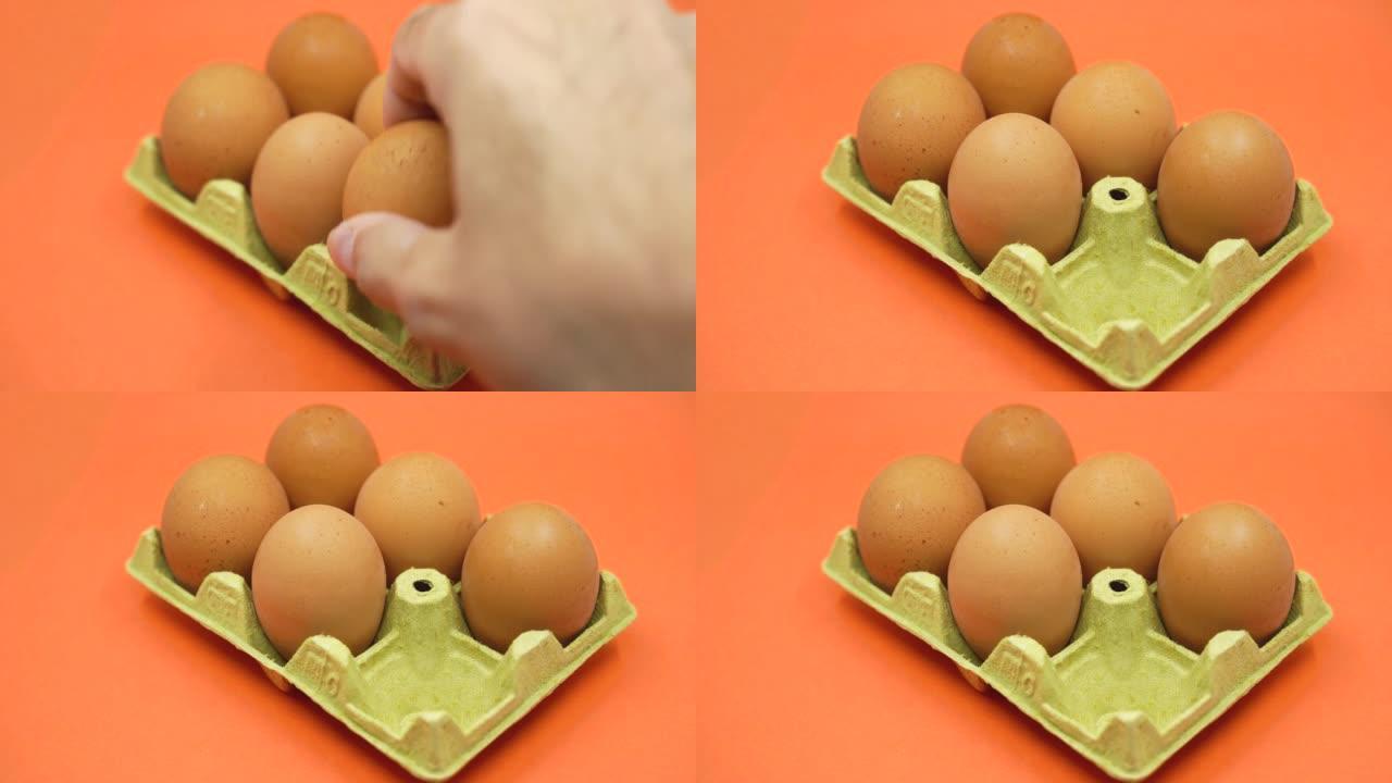 用手从橙色背景上打开的鸡蛋纸箱中取出鸡蛋。收缩概念。