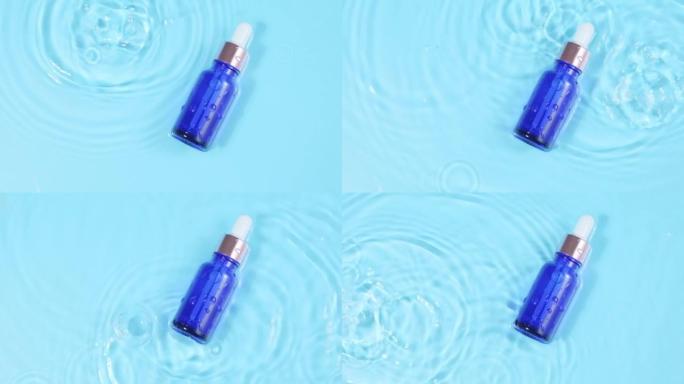 广告慢动作，带移液器的玻璃化妆品瓶位于水面。水滴的俯视图落入水中，蓝色背景上的水圈发散。设计包装