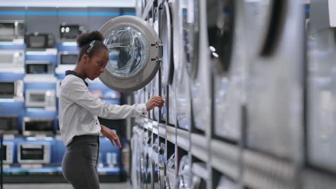 美国黑人妇女正在查看洗衣机，选择新的洗衣设备，交易大厅访客的中型肖像照片