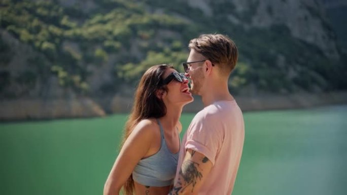 可爱的年轻夫妇站在美丽的绿松石湖边接吻
