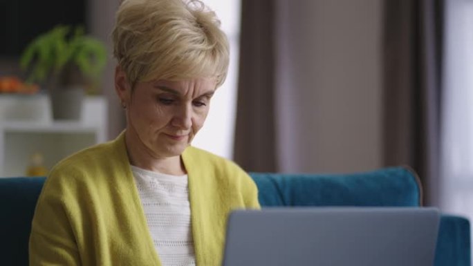 好看的老妇人正在家里远程工作，使用笔记本电脑发送信息，在键盘上键入文本，在互联网上自由职业