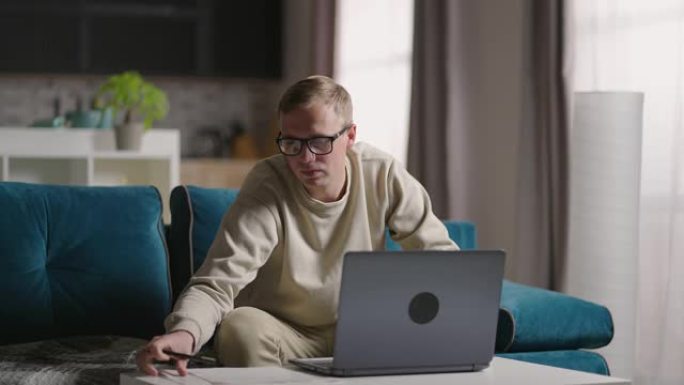 严肃的年轻人自由职业者在家自由职业者在笔记本电脑上打字电子邮件，专注的人在家坐在沙发上在线学习电脑，