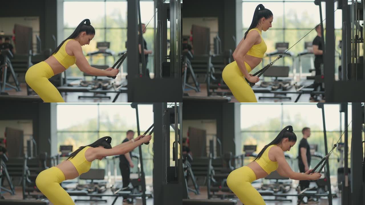 一位穿着黄色运动服的年轻西班牙裔妇女在交叉运动中进行锻炼，从上方拉一根绳子训练背部和肩膀。黑发女人在