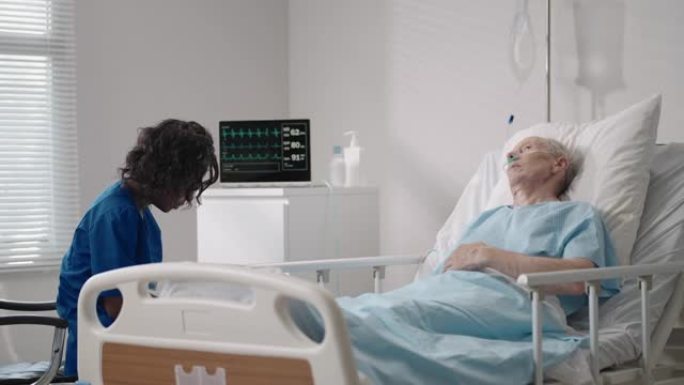 一位皮肤黝黑的女医生正在和一位躺在病床上的老年男性患者交谈，讨论康复后的康复。