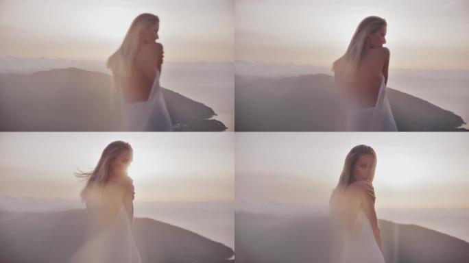 美丽的天真无邪的云朵女神，金色的头发裹着白色的长袍，顶着夕阳站在山顶上，用相机调情
