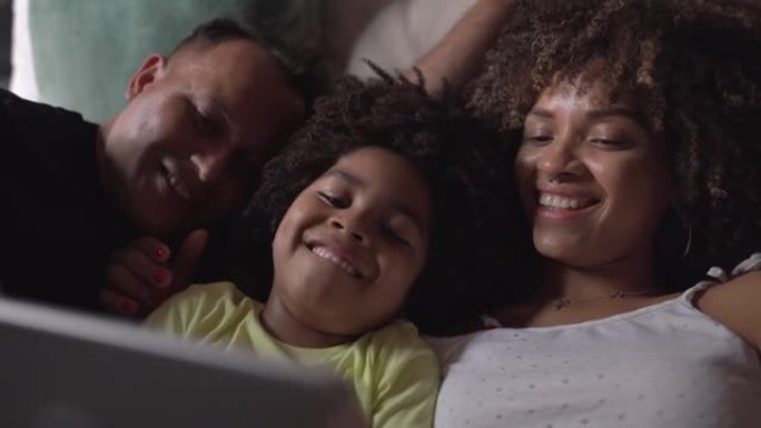 一家人躺在床上在家用数字平板电脑观看视频或电影