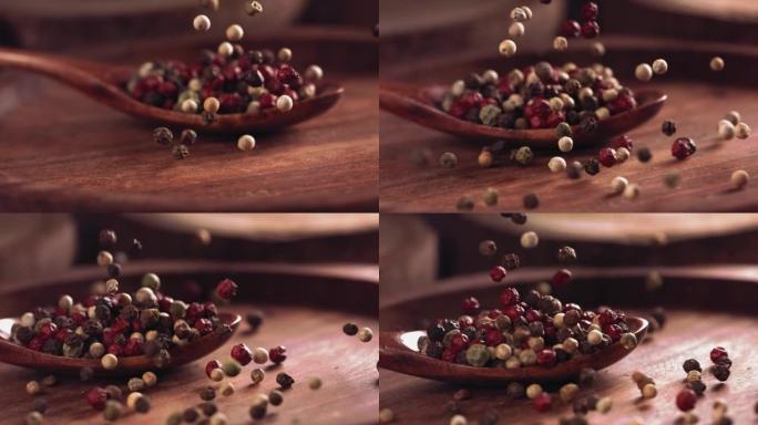 五颜六色的胡椒落在木勺桌上。慢动作。特写
