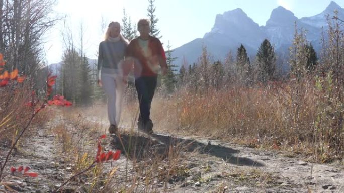 成熟的夫妇沿着秋天的高山小径行走，遥远的山脉