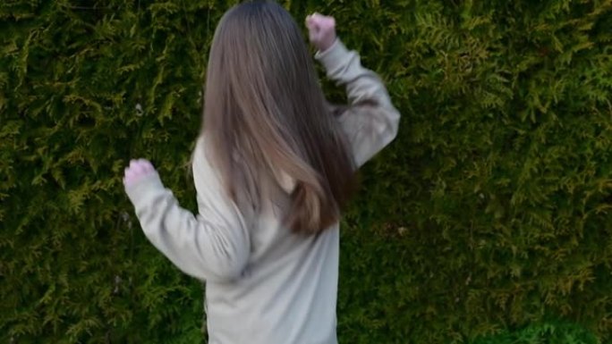 一个穿着米色西装的可爱女孩在户外跳舞的慢动作视频，快乐的孩子在花园里跳舞