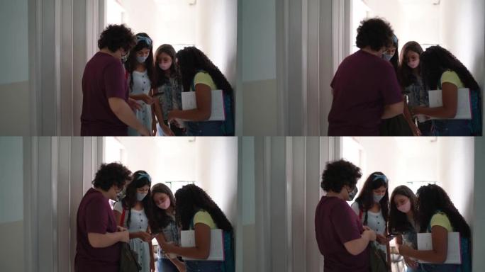 一群朋友在学校的走廊里聊天和使用手机-戴口罩