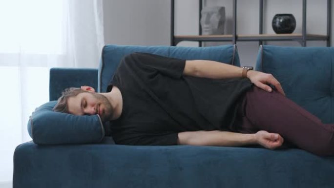 疲惫的男人在家里躺在蓝色的沙发上睡觉，努力工作后乏力，懒惰的周末