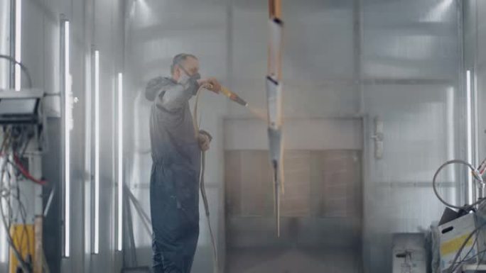一个戴着呼吸器的人正在用粉末法涂金属。钢铁和金属结构的生产。画店。画家用喷枪油漆工作