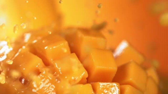 通过芒果立方体切片飞溅的芒果汁的慢动作镜头